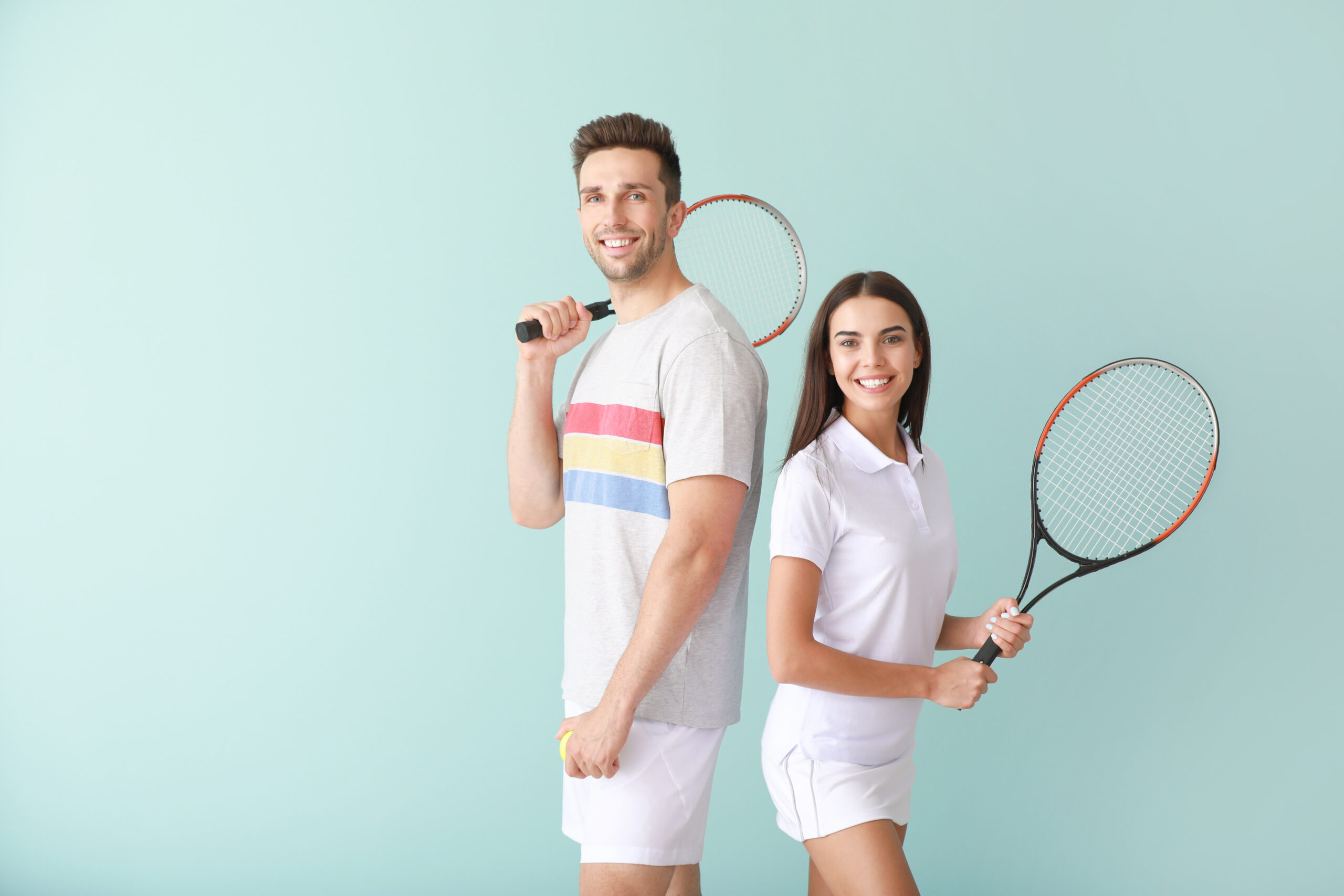 Young couple with tennis rackets on color background